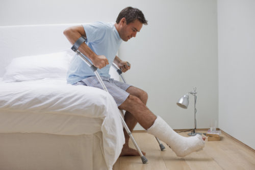 A man with a broken leg using crutches to get out of bed. 