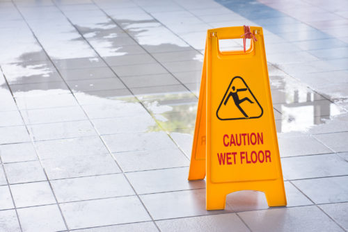 A wet floor sign by a puddle on a walkway.