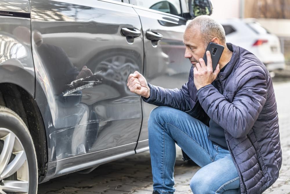 A man inspects his damaged car and wonders what happens after a car accident that is your fault. 