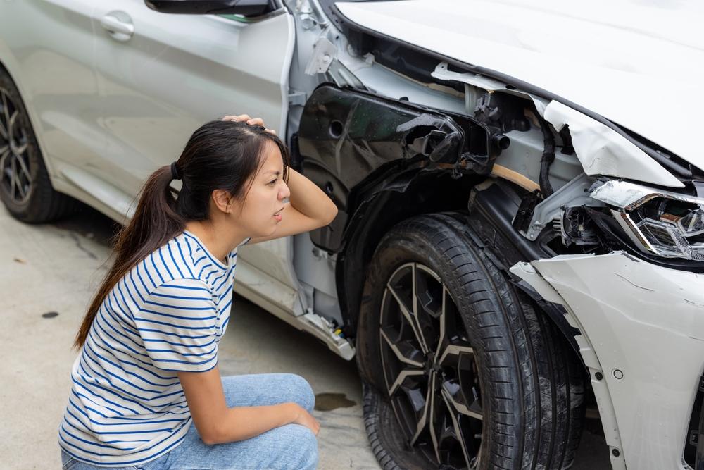 A woman inspects her damaged car and wonders whose insurance pays in a multi-car accident. 